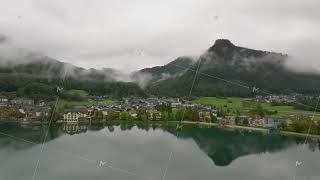 Low clouds blanket the lush green slopes of the Alps enveloping a quaint Austrian town by the [upl. by Cohleen734]